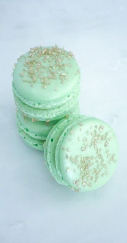 three green macaroons with gold sprinkles on them sitting next to each other