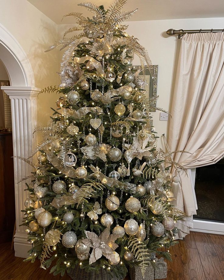 a decorated christmas tree in a living room with gold and silver ornaments on the top