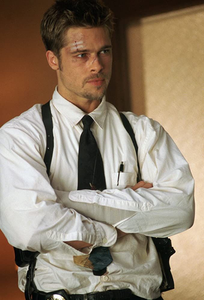 a man wearing suspenders and a tie standing with his arms crossed