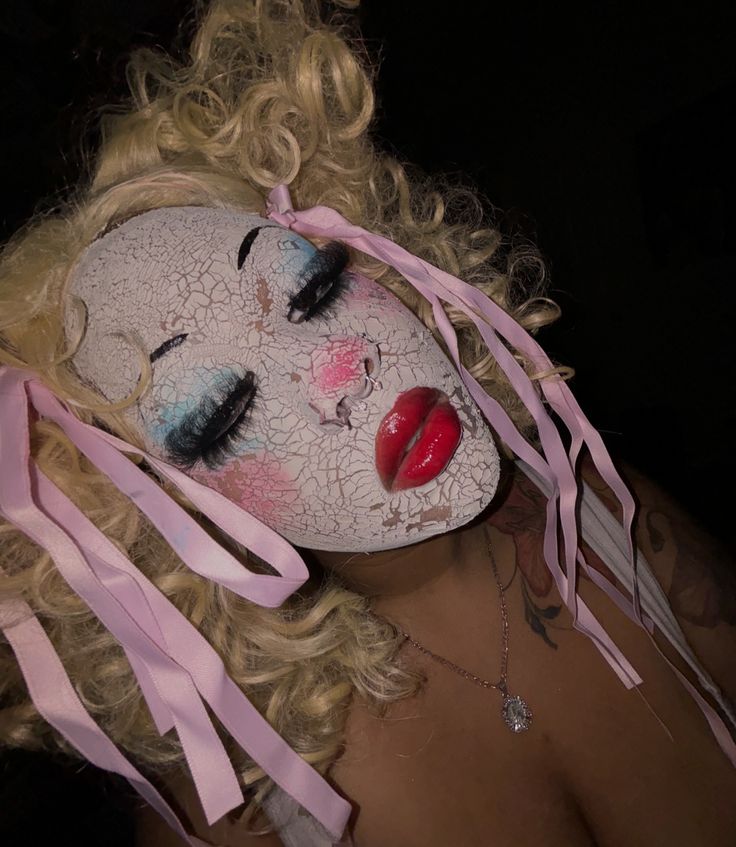 a woman with blonde hair wearing a white mask and pink ribbon around her neck,