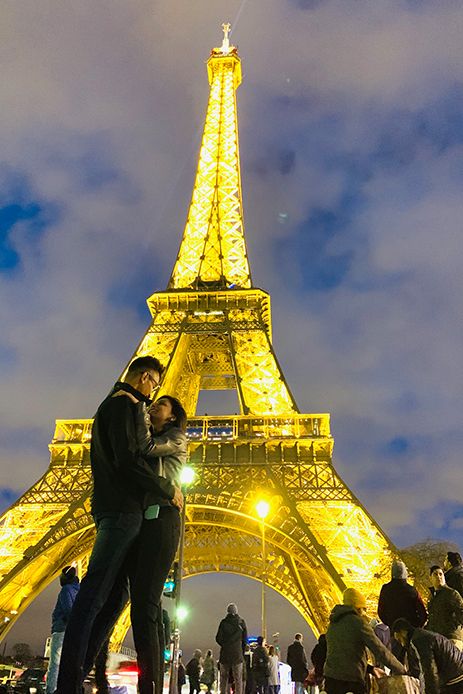 two people standing next to each other in front of the eiffel tower at night