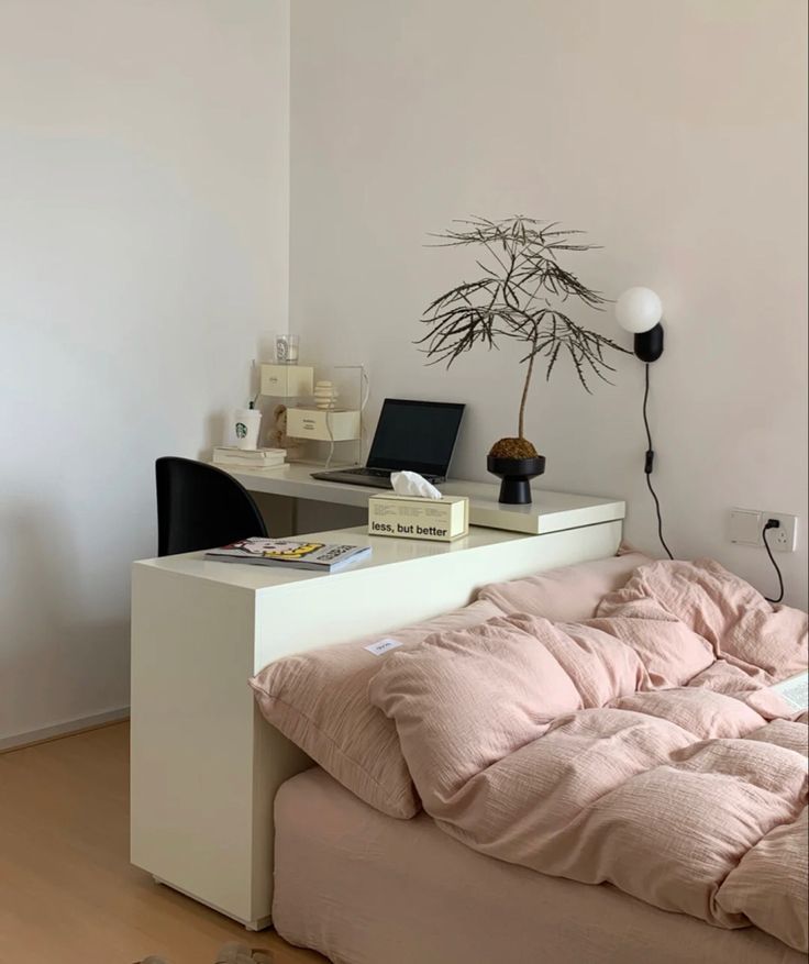 a bed with a pink comforter on top of it next to a computer desk