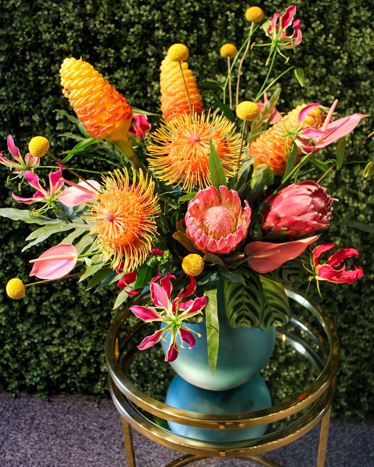 a blue vase filled with lots of flowers on top of a table next to a green wall