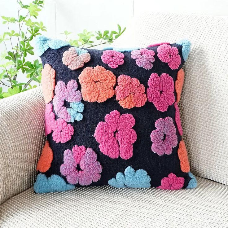 a black and pink flowered pillow sitting on top of a white couch next to a potted plant