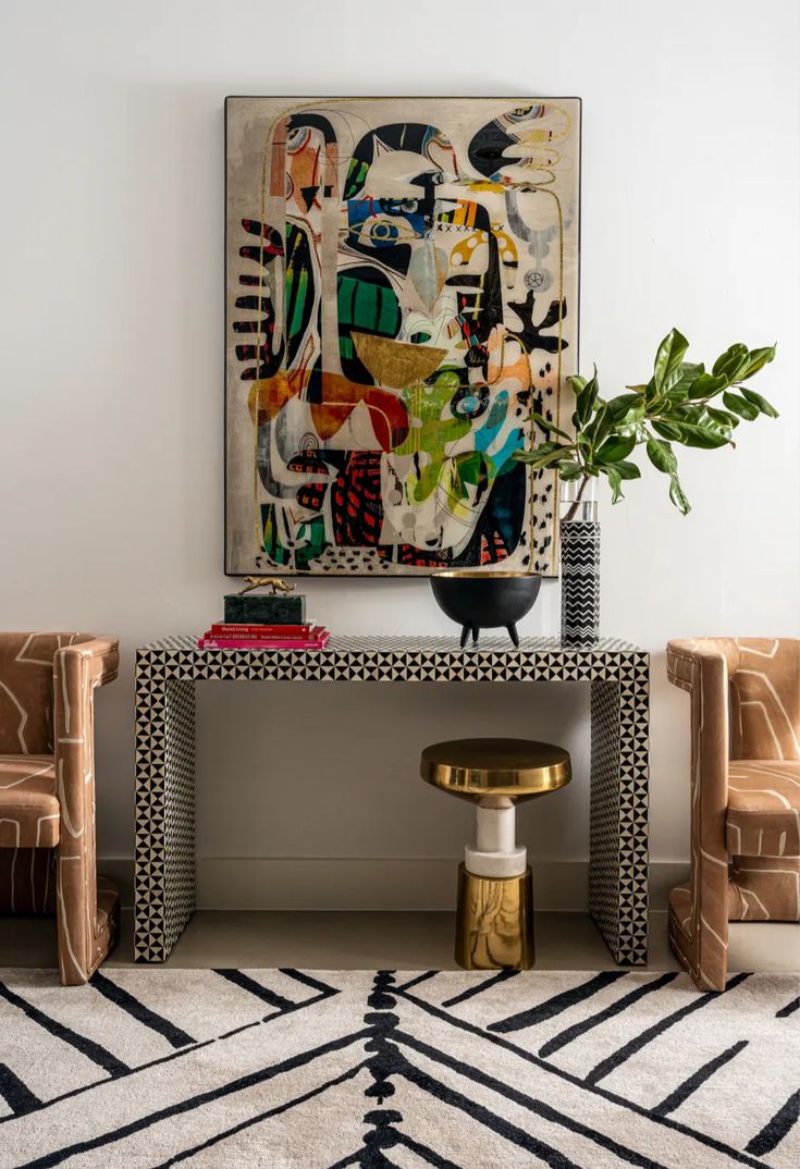 a living room with two chairs and a large painting on the wall above it's console table