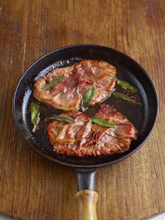 three pieces of meat cooking in a skillet on a wooden table with a spatula