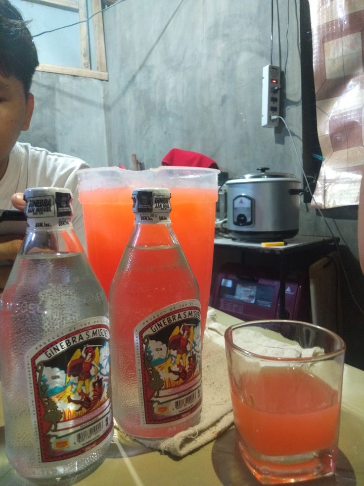 two bottles of alcohol sit on a table next to a glass and a bottle of orange juice