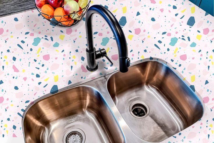 two stainless steel sinks in a kitchen under a faucet with colorful wallpaper