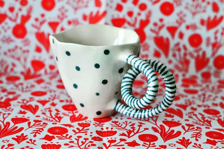 a white cup with black and red designs on it sitting on top of a table