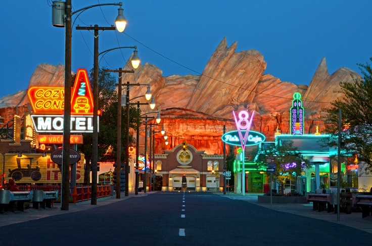 an image of a street at night with neon signs on the buildings and mountains in the background