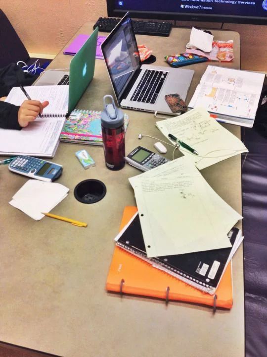 a person sitting at a table with two laptops and papers on top of it