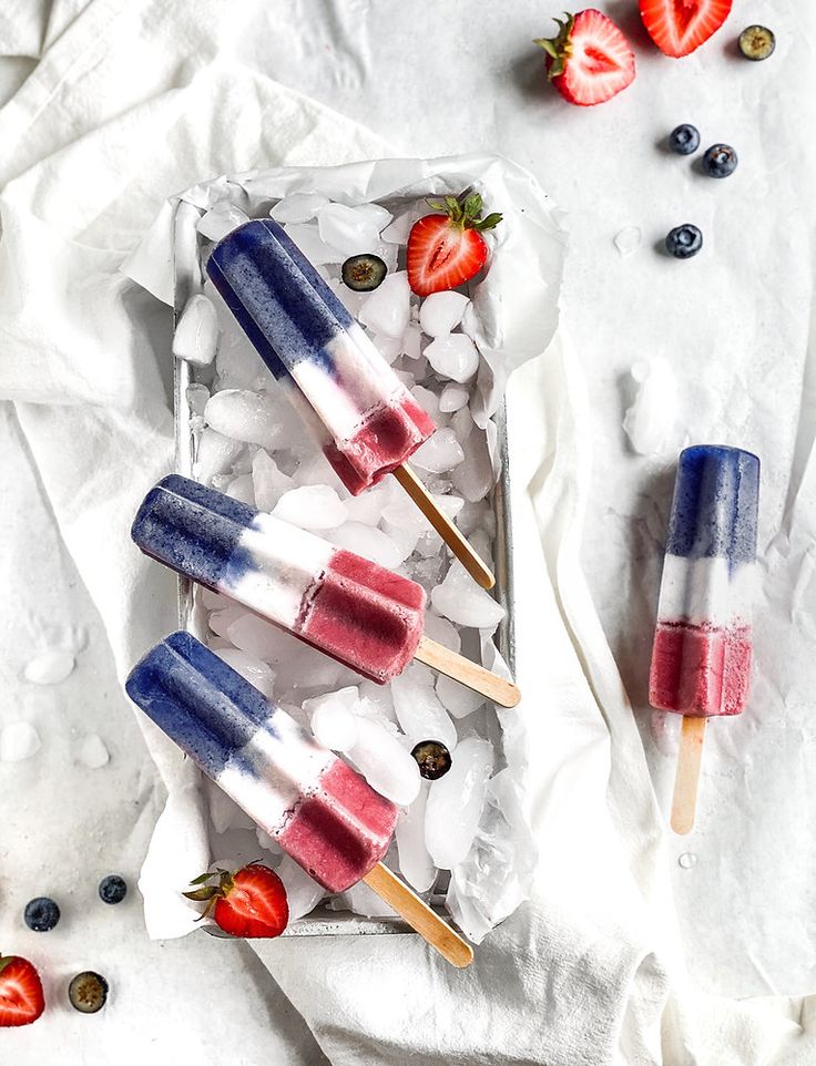 three popsicles with strawberries and ice cream on them sitting in an ice tray