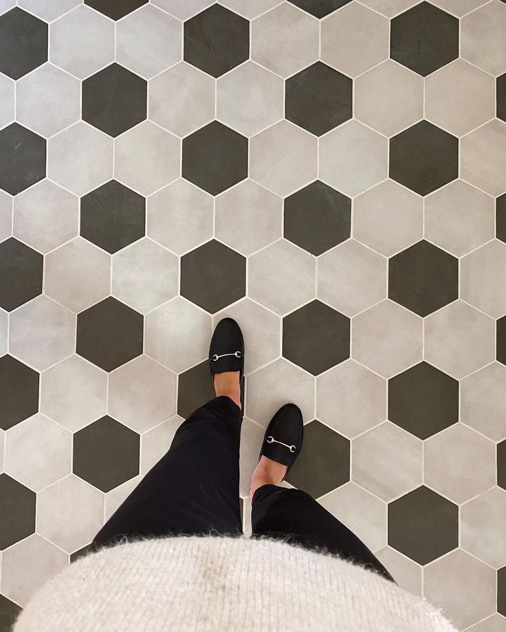 a person wearing black shoes standing in front of a tiled floor with hexagonal tiles