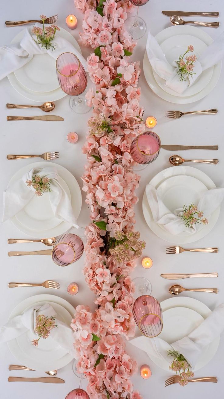 the table is set with pink flowers and gold place settings for an elegant dinner party