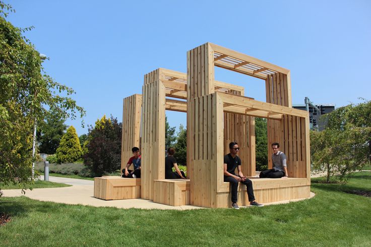 two men sitting on wooden benches in the grass near a building made out of wood