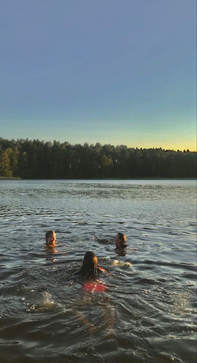 three people swimming in the water with trees in the background