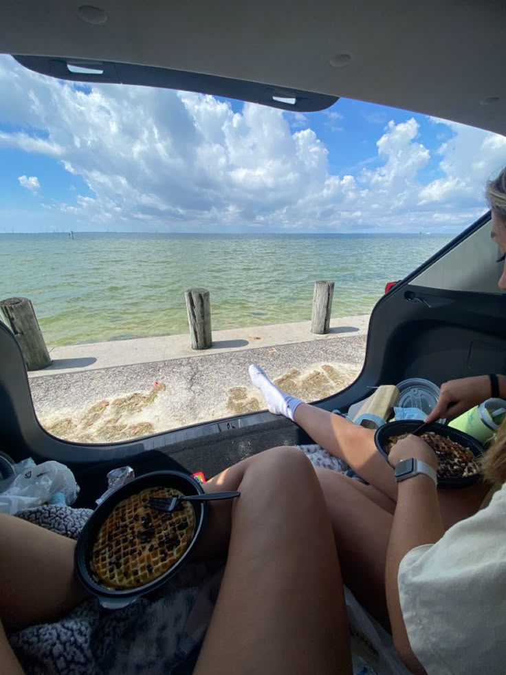 two women are sitting in the back of a vehicle with food and drinks on it