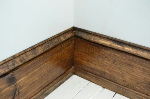 the corner of a room with wood flooring and white painted walls, along with wooden planks