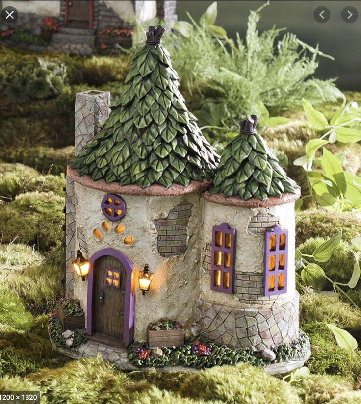 a fairy house is shown in the middle of some mossy plants and bushes with lights on it