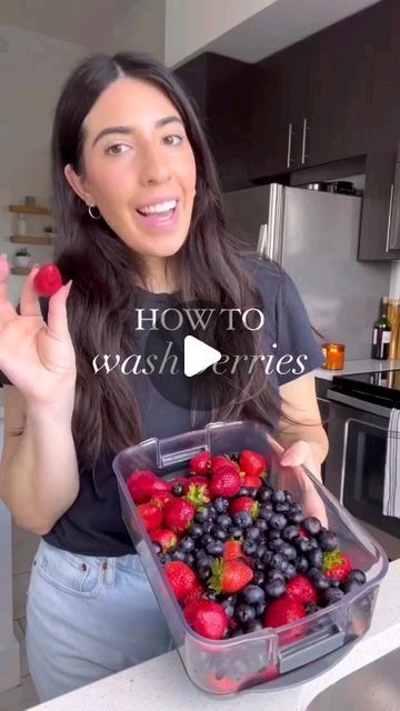 a woman holding up a plastic container filled with berries