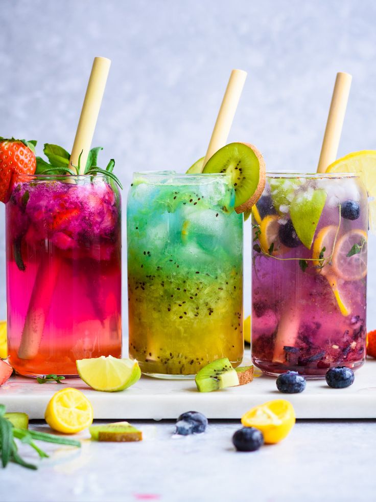 three different colored drinks with strawberries, lemons and blueberries on the side