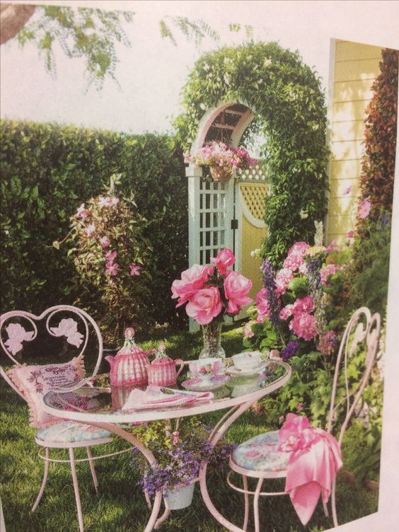 a table and chairs with pink flowers in the back ground, near a garden area