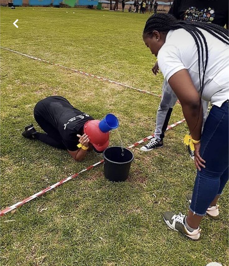 two people in the grass with buckets on their feet and one person holding a water bottle