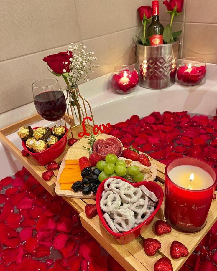 a bath tub filled with lots of food next to a candle and some flowers on the floor