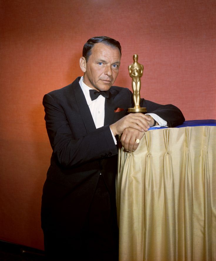 a man in a tuxedo holding an oscar statue