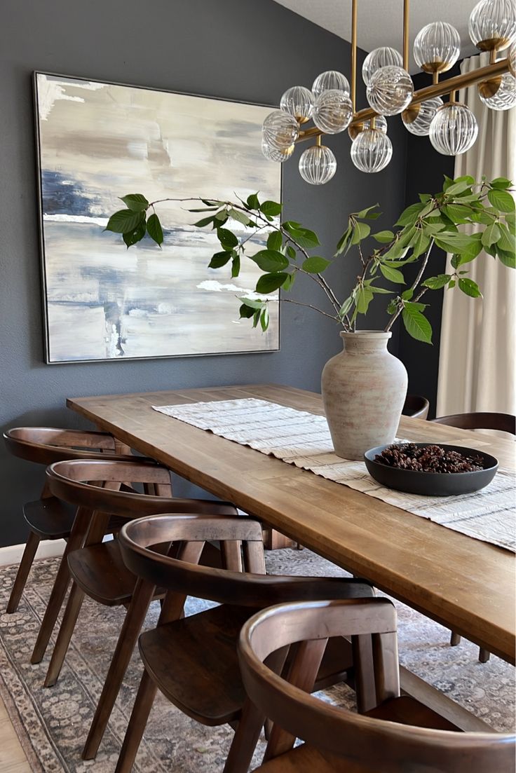 a dining room table with chairs and a vase filled with plants on top of it