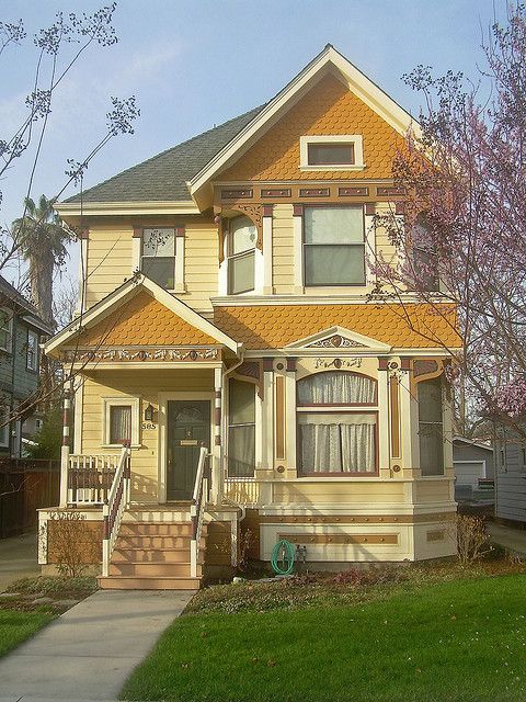 a yellow house with brown trim on the front porch and stairs to the second floor