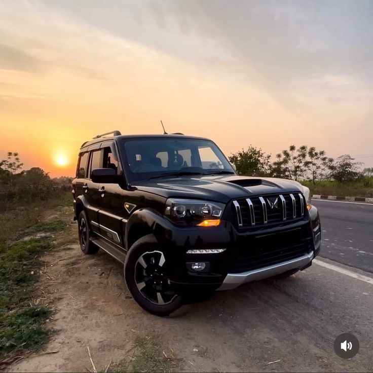 the jeep is parked on the side of the road near the grass and trees at sunset