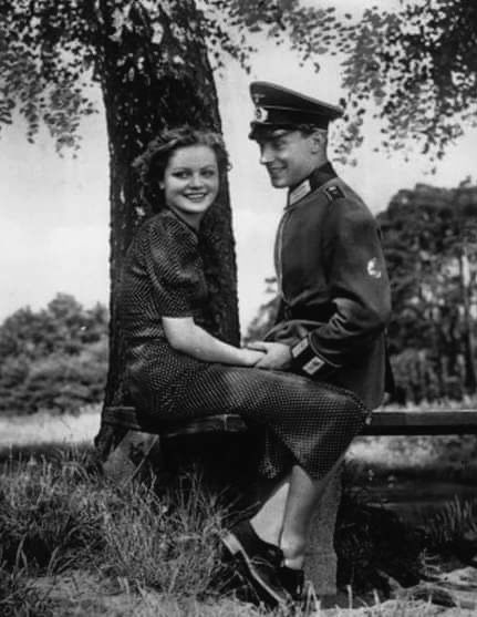 an old black and white photo of two people sitting on a bench near a tree