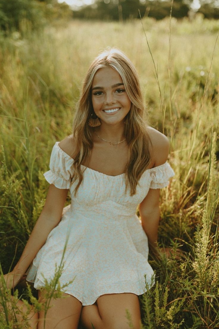 a woman sitting in tall grass smiling at the camera