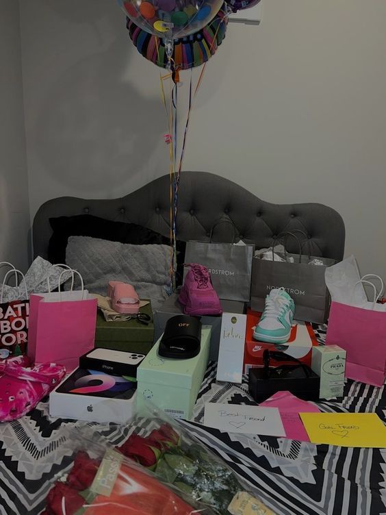 a bed topped with lots of boxes and balloons next to a table filled with gifts