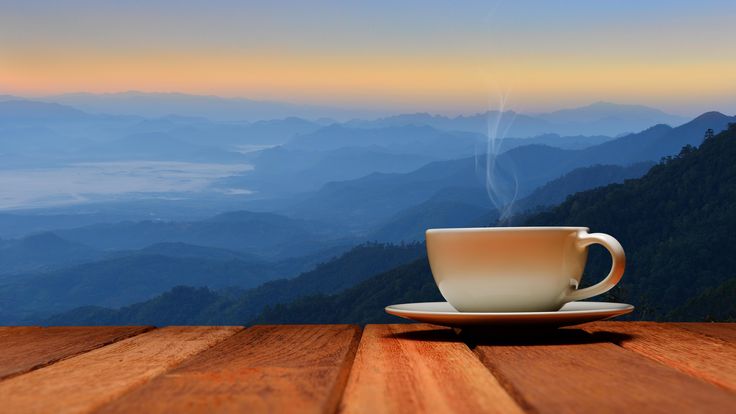 a cup of coffee sitting on top of a wooden table next to a mountain range