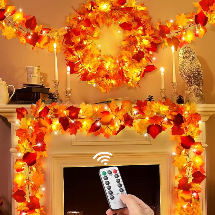 a person is holding a remote control in front of a fireplace decorated with fall leaves