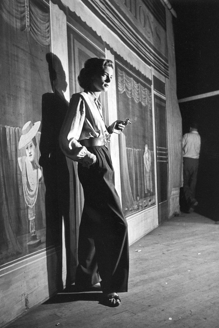 black and white photograph of woman leaning against wall with cell phone in hand, looking at screen