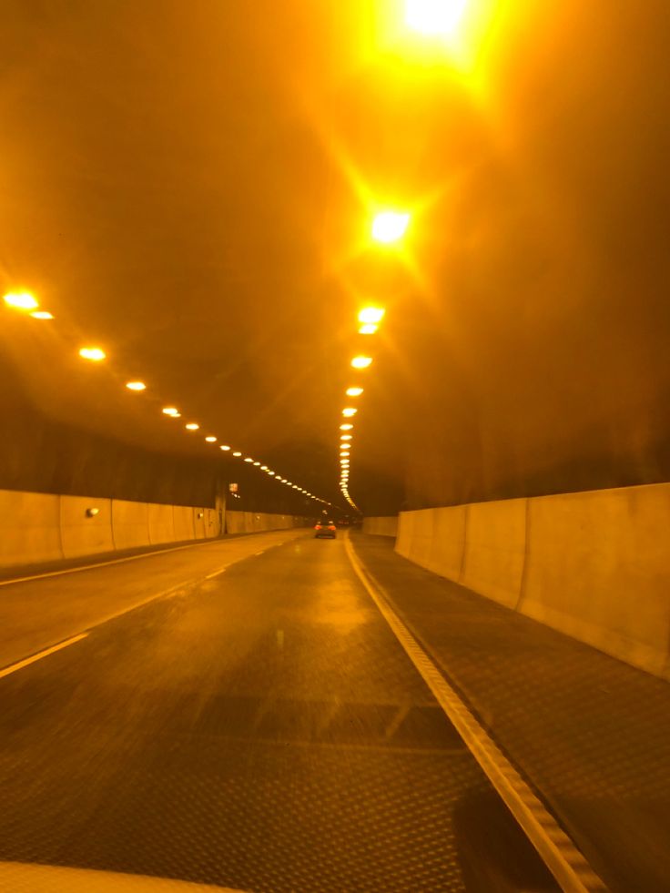 an image of a car going down the road at night time with lights on in the background