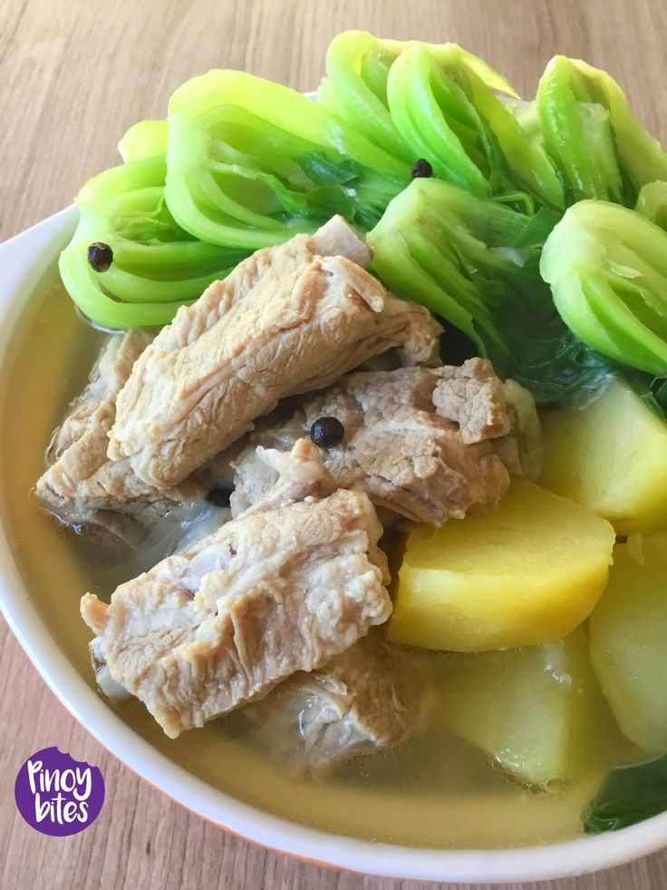 a white bowl filled with meat and vegetables on top of a wooden table next to sliced cucumbers