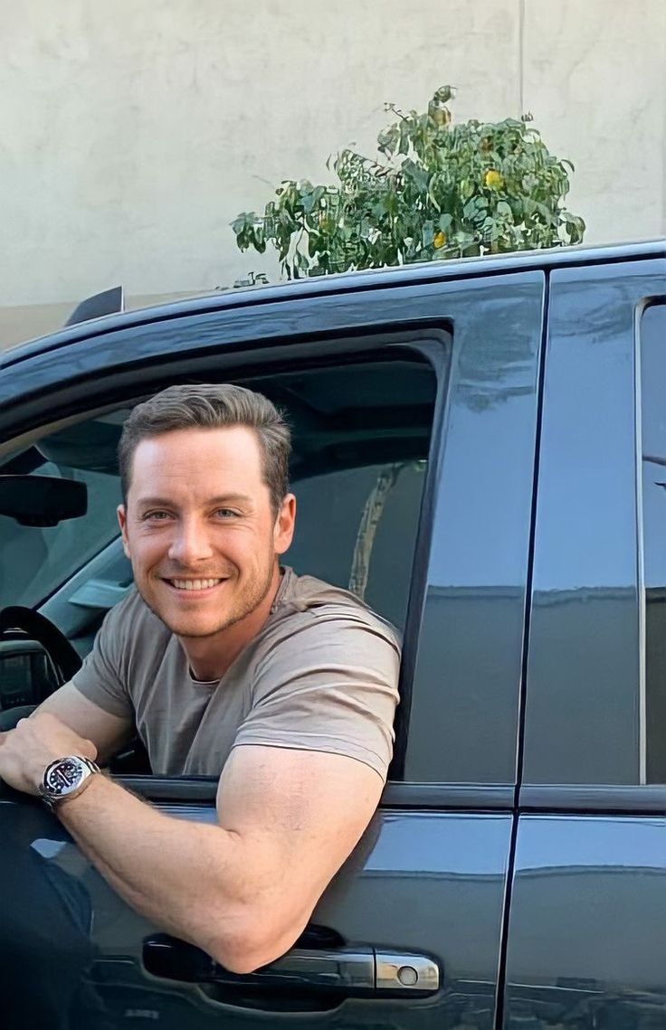 a man sitting in the drivers seat of a black car with his hand on the door handle