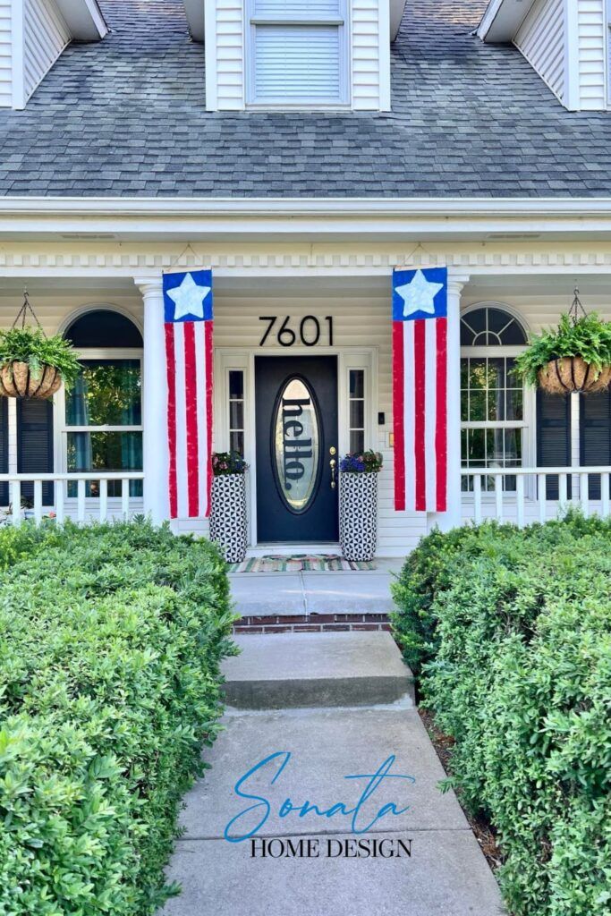 an american flag painted on the front door of a house with bushes and shrubs around it