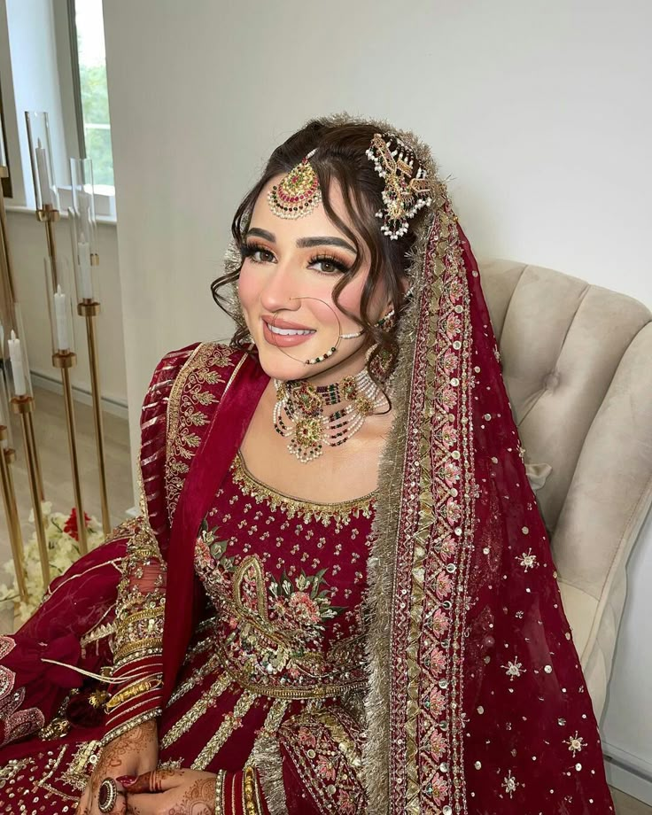 a woman in a red and gold bridal outfit sitting on a chair with her eyes closed