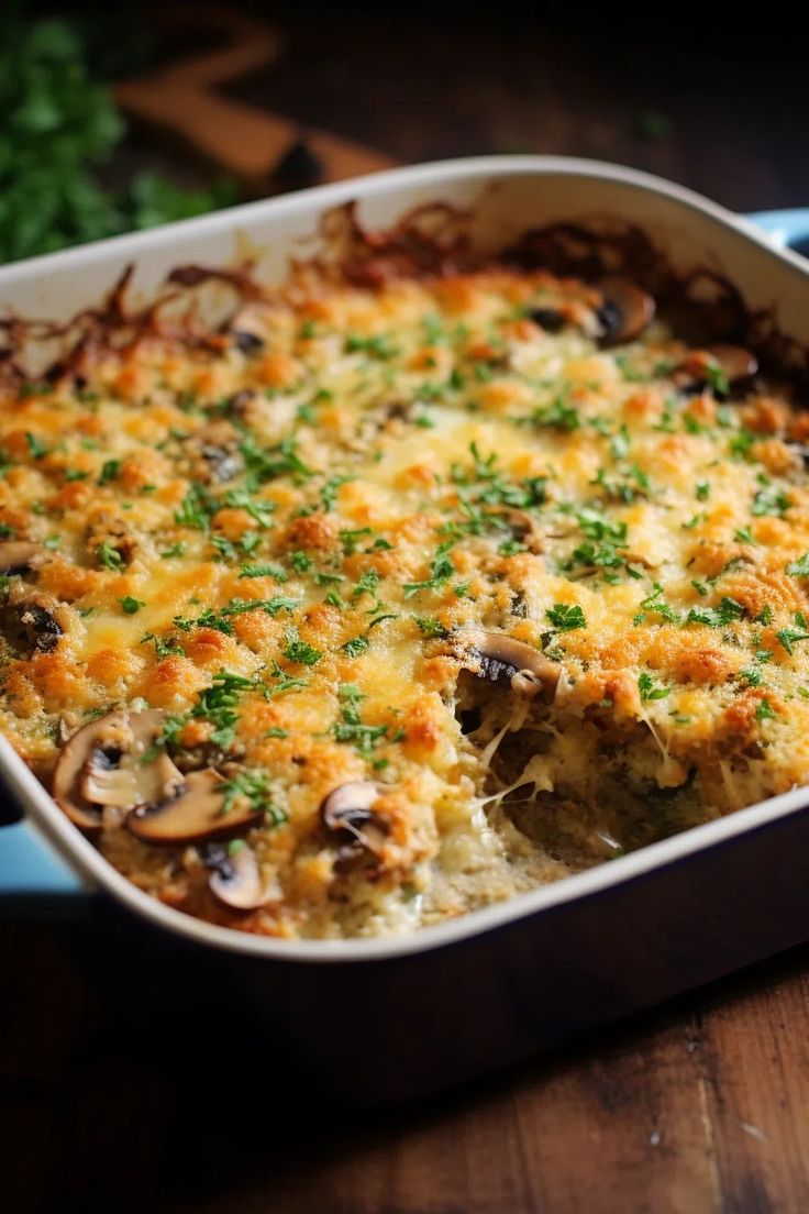 a casserole dish with mushrooms, cheese and parsley in it on a wooden table