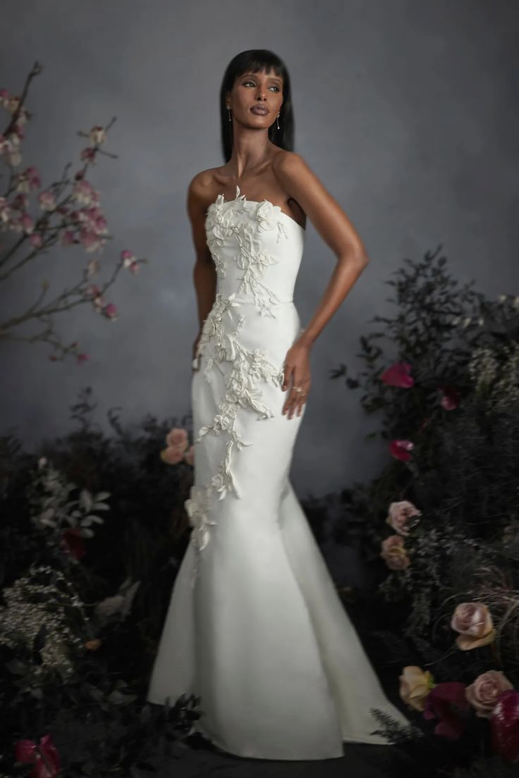 a woman in a white dress standing next to flowers