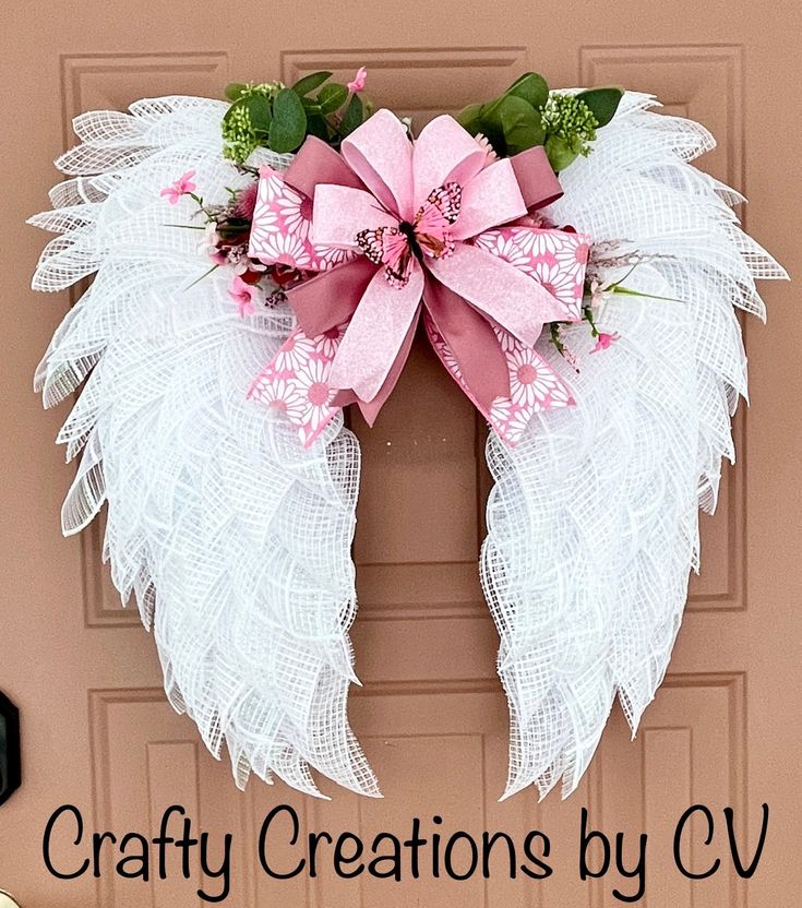 a pink and white wreath with angel wings on the front door to a house that says crafty creations by cv