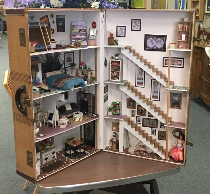 an open dollhouse with stairs and pictures on the walls, sitting on a chair