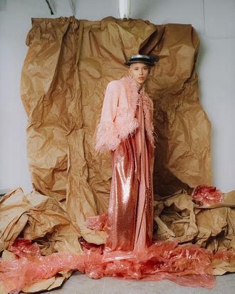 a woman in a pink dress and hat standing on some brown paper with her hands behind her back