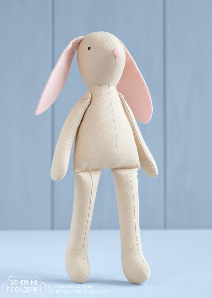 a beige stuffed animal with pink ears on it's head, standing in front of a blue background