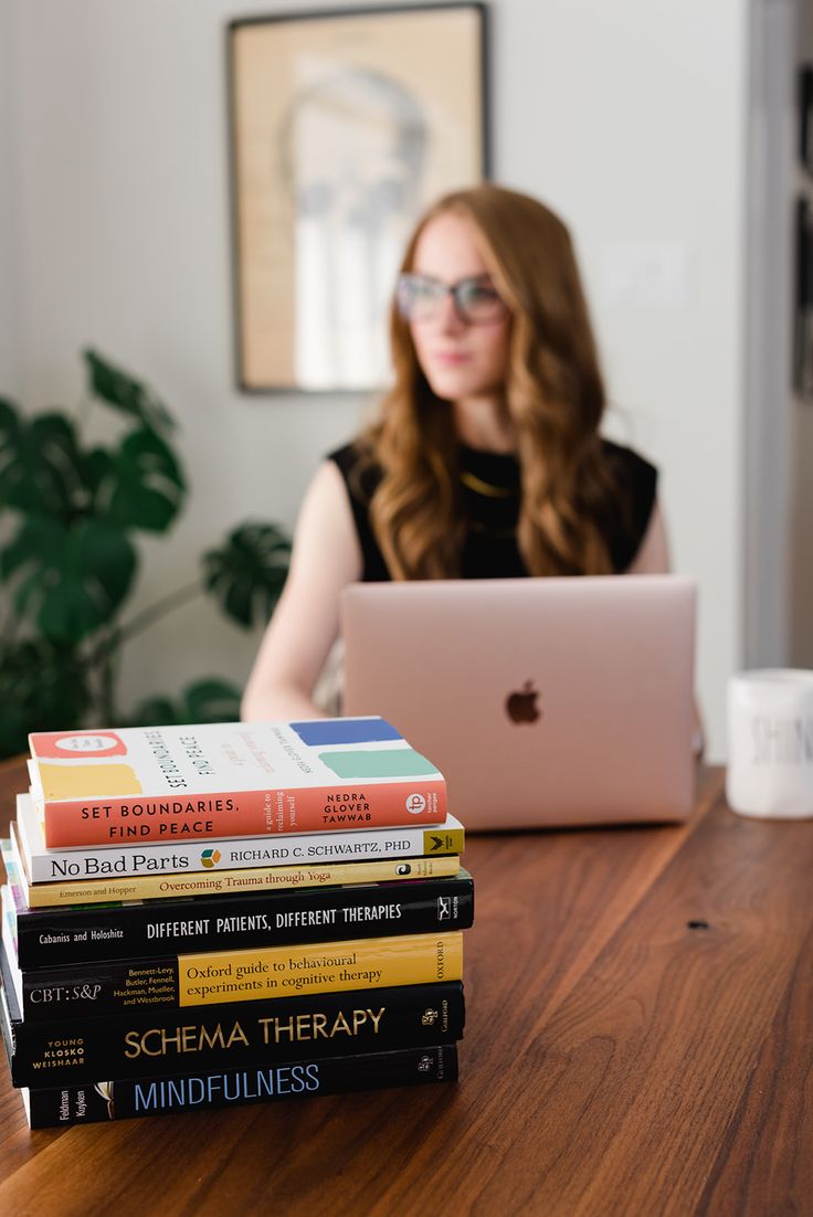 a woman sitting at a table with a stack of books in front of her laptop